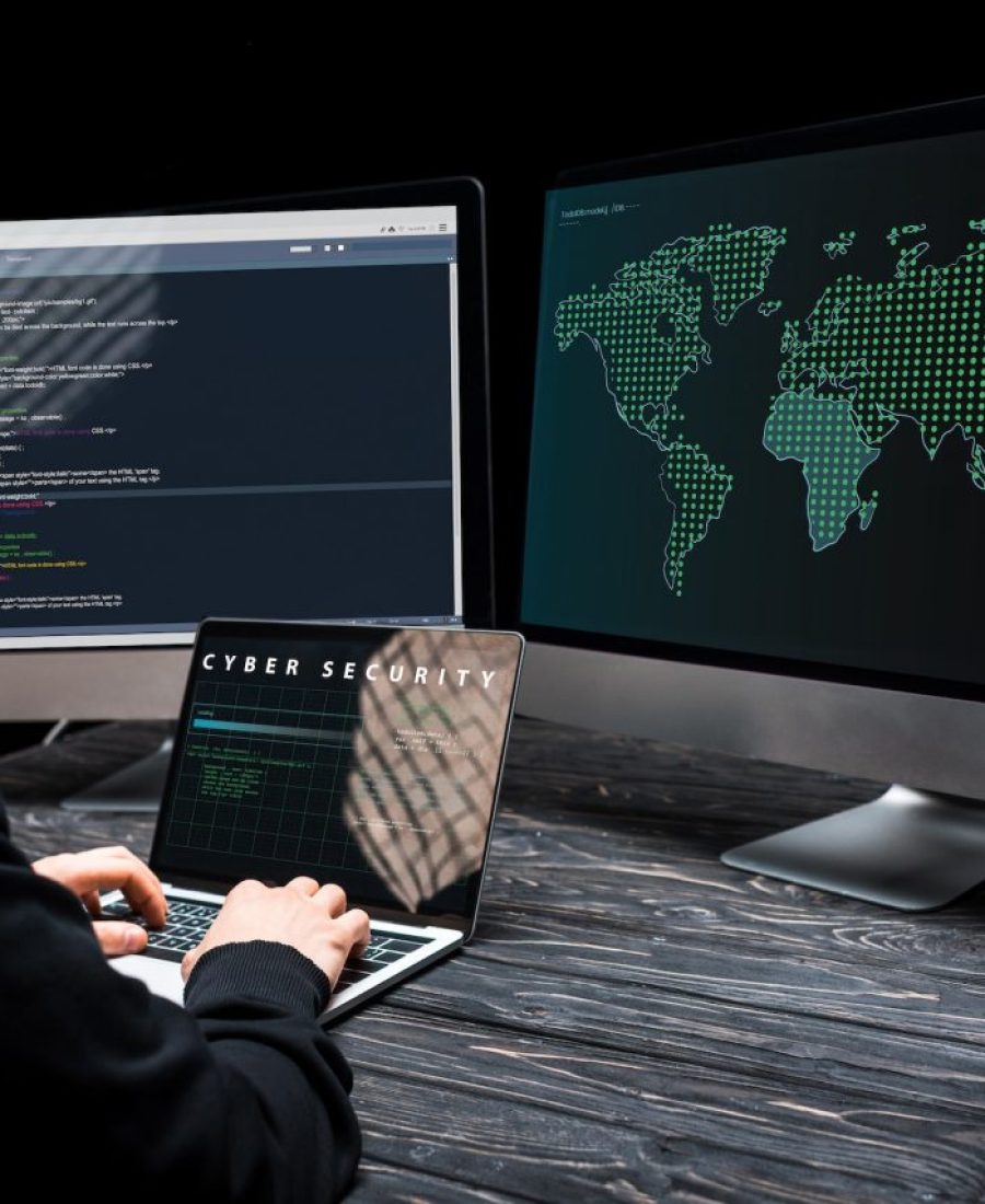 hacker-using-laptop-with-cyber-security-lettering-on-screen-near-computer-monitors-on-black.jpg