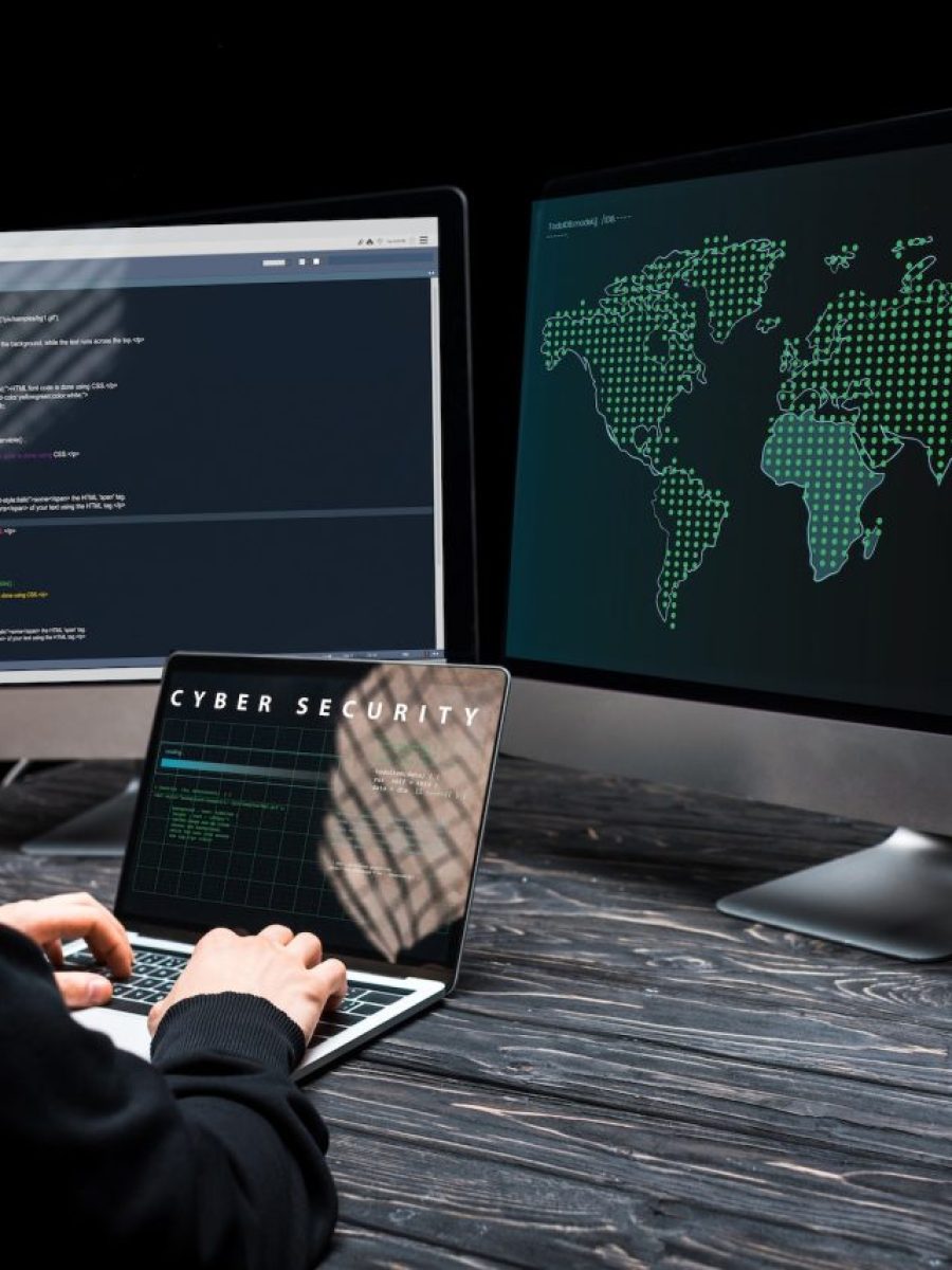 hacker-using-laptop-with-cyber-security-lettering-on-screen-near-computer-monitors-on-black.jpg